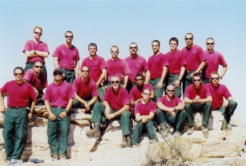 A fire crew wearing red shirts and green Nomex pants poses on a flat rock.