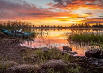 A blue boat is moored on the banks of a calm river under a colorful sunset