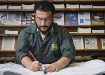 An employee in uniform marks up some large documents inside a Forest Service office