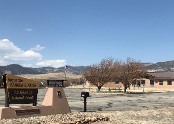 A brown and yellow sign depicts the Saguache Ranger Station from the front of the parking lot.