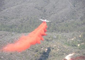 aerial photo showing a white airplane dropping a cloud of red fire retardant over a forested area