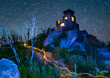 looking up at a lit-up lookout tower on a dark starry night