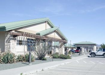 Tan building with green metal roof and parking area.