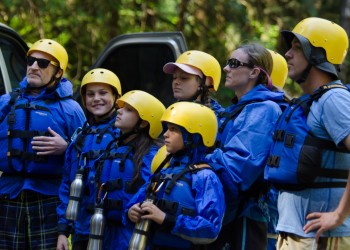 Group of people wearing matching life vests and helmets for whitewater rafting.