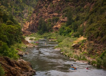 A river flows through a canyon and multiple rafts float down it.