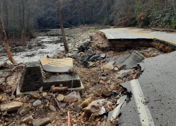 Broken asphalt and destroyed road with Mount Rogers National Recreation Area sign on the ground next to a river