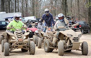 Riders covered in mud sit on OHVs smiling