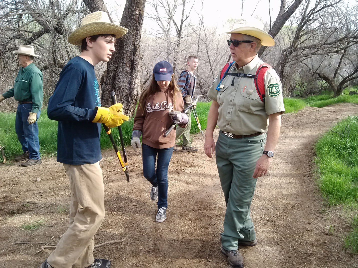A man wearing a Forest Service uniform is with several Eagle Scouts repairing trails on the forest.