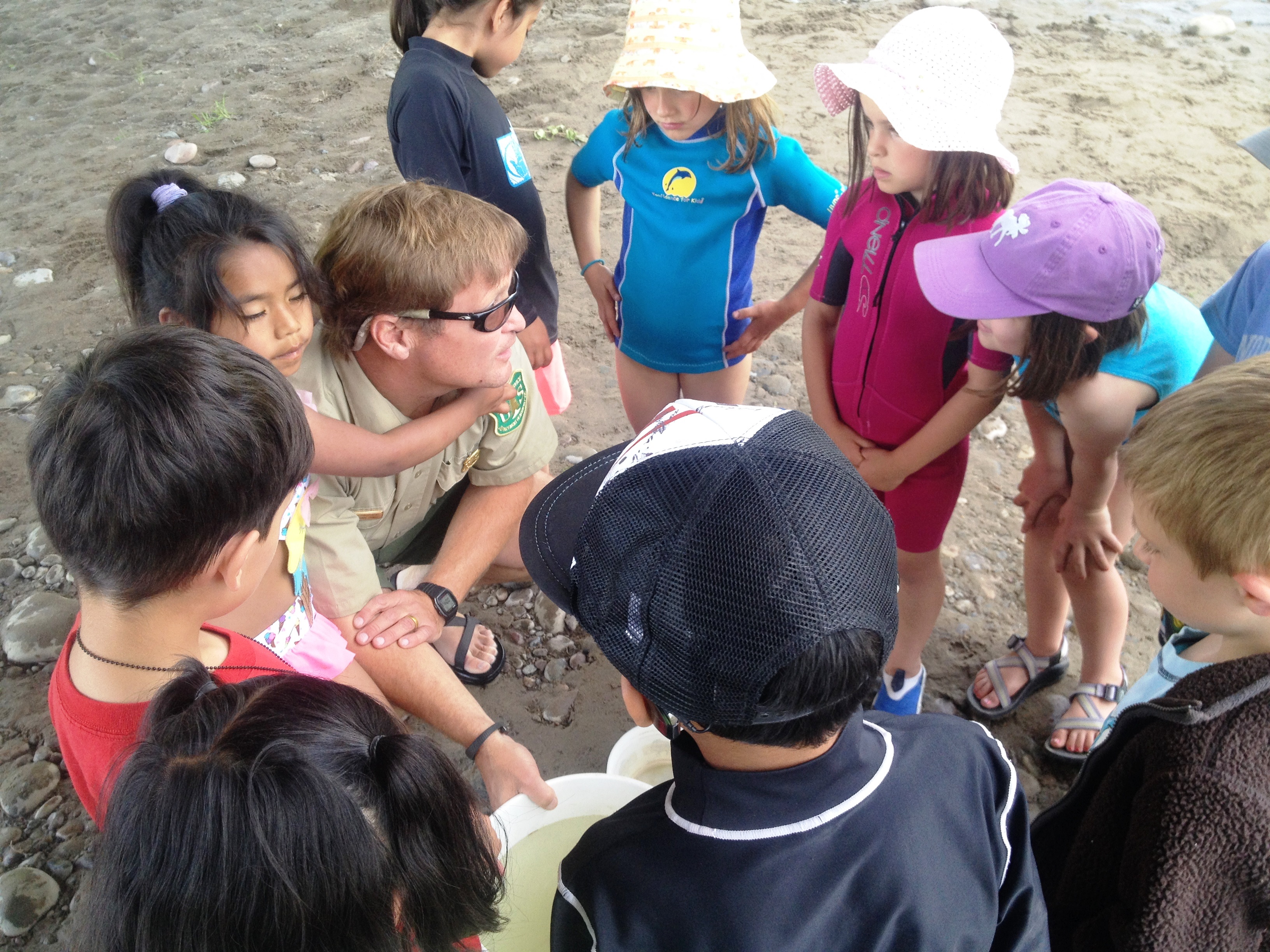 Elementary school children gather around a Forest Service employee outside.