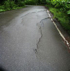 Tension cracks in asphalt surface due to embankment settlement.