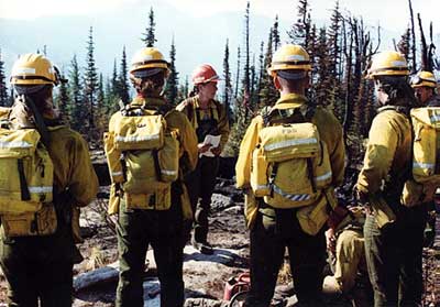 A photo of a group of wildland firefighters in full gear listening to their crew boss.