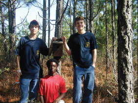 Photo of three teens posing in front of a nest box they just completed installing. 