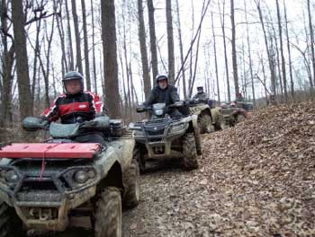 Photo of an ATV club volunteering to help maintain trails. In the photo the club memebers are riding their ATVs along a forested trail.