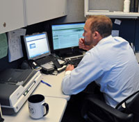 A man at a cubicle desk looks at a monitor screen.