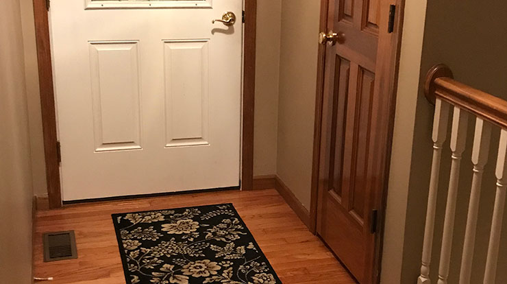 Interior of a home entrance showing wood floors, wood door, wood bannister, and trim.