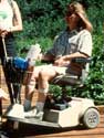Photo of a woman using a motorized, 3-wheeled "scooter" type wheelchair.