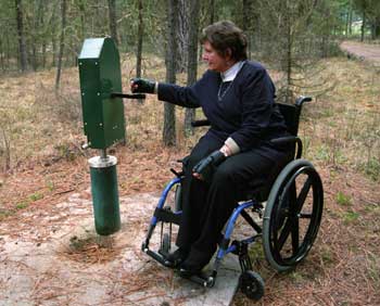 Photo of a woman operating an accessible handpump at a campground site.