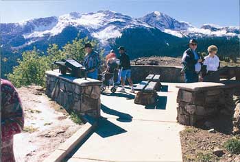 Photo of several people with and without disabilities, at a scenic overlook with mountainous vistas surrounding them.