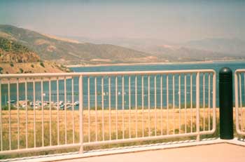 Photo of a painted steel pipe guardrail around a viewing area. The view of boats on the water is clearly visible through the vertical rails.