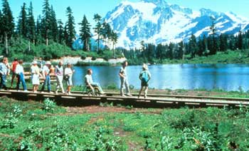 Photo of several people, with and without disabilities, on a raised boardwalk beside an alpine lake.