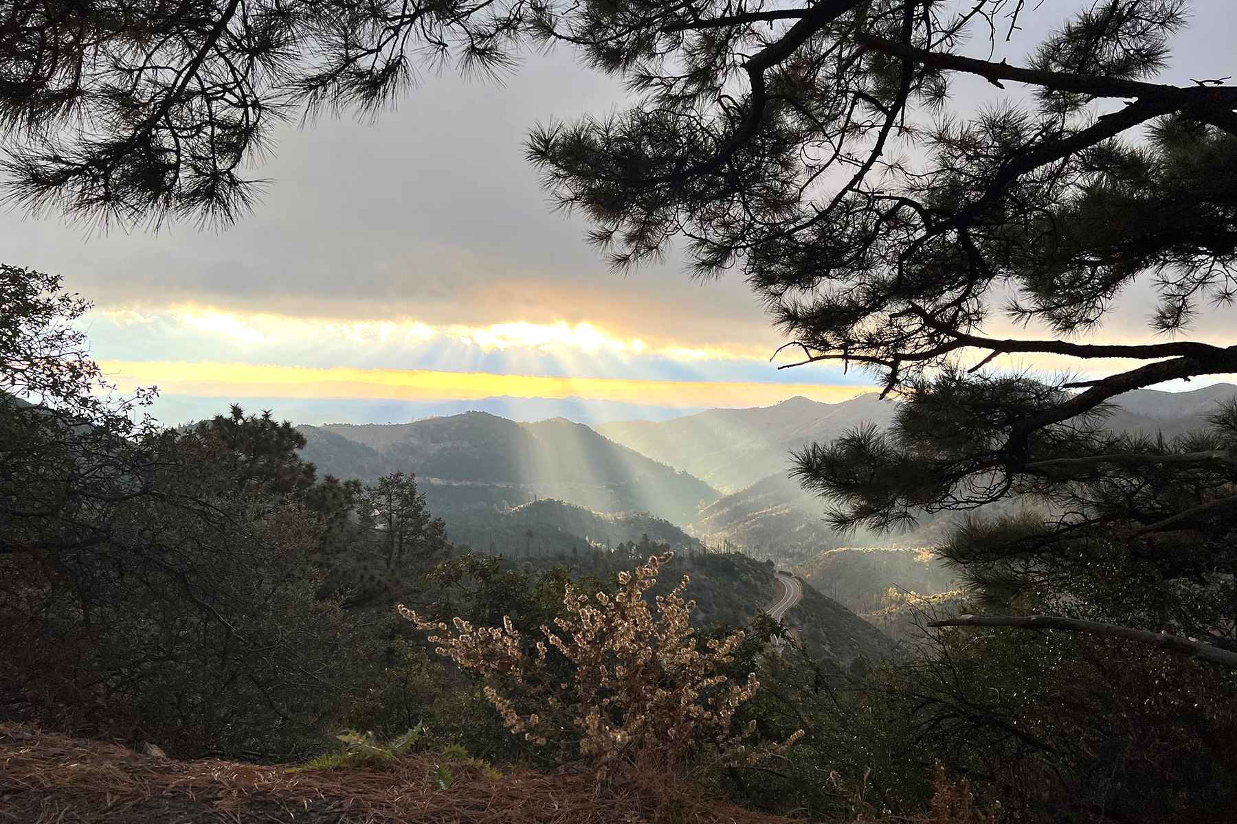 The sun rising over mountains, behind clouds, creating multiple sunbeams.