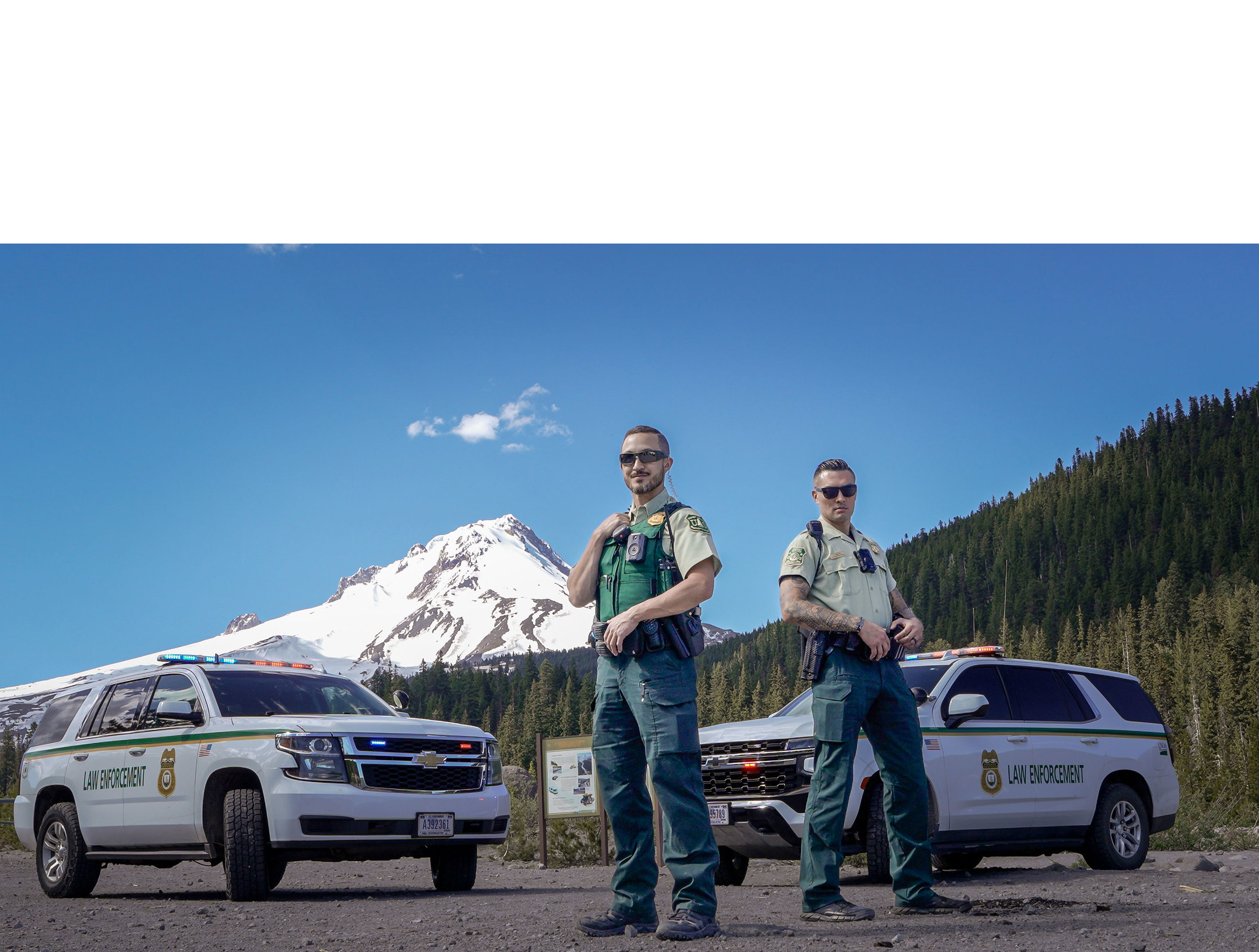 Two law enforcement officers standing in front of two law enforcement vehicles
