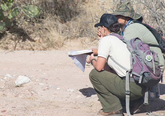 A picture of two employees crouched down on dirt road.