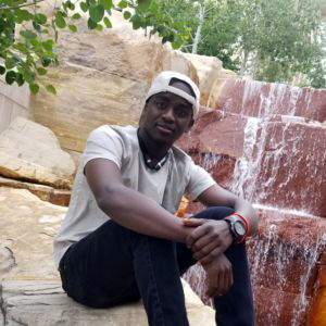 Abdusalam Ibrahim perched on a boulder in front of waterfall.