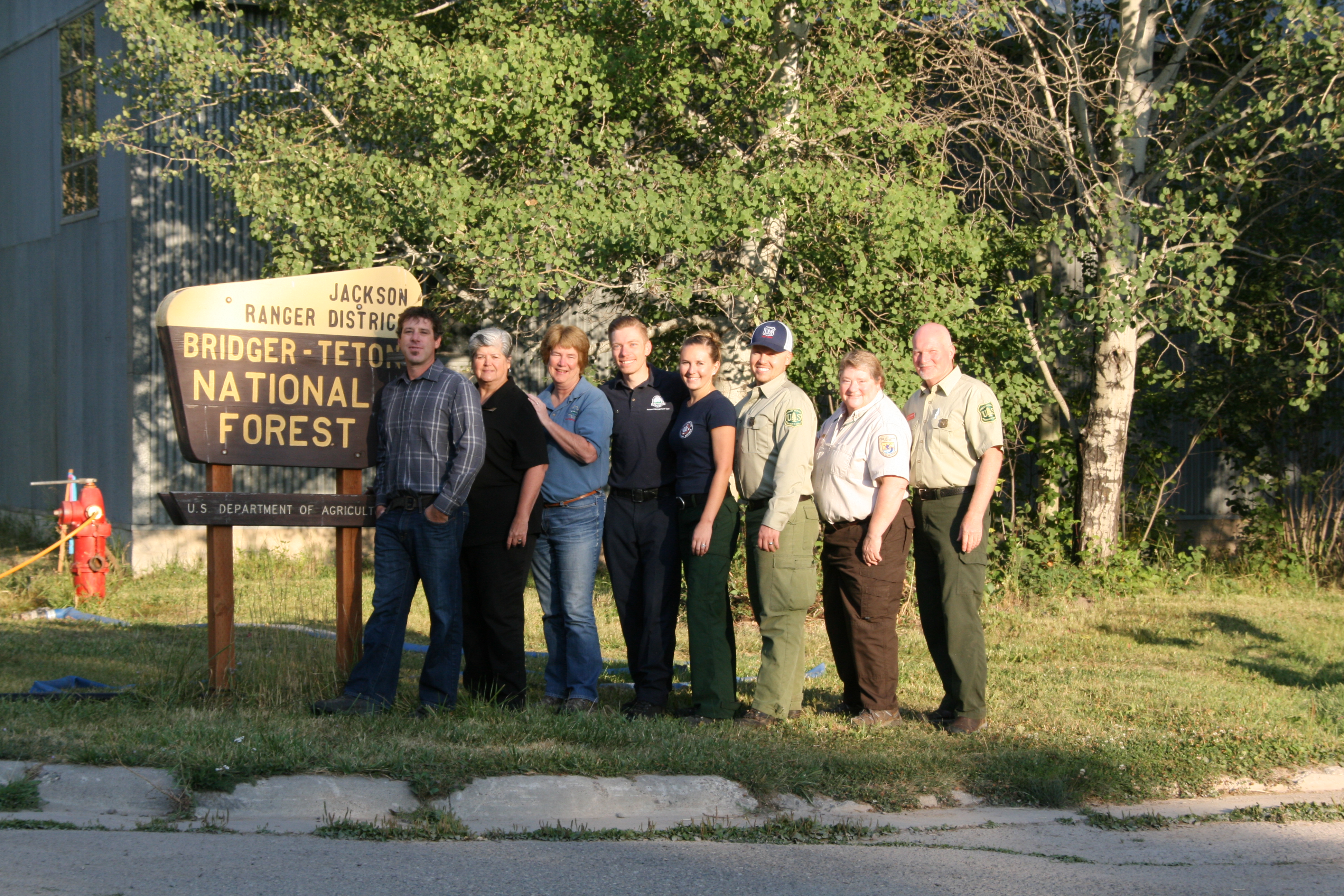 People standing beside each other in a line, next to the USDA Forest Service, Jackson Ranger District, Bridger-Teton National Forest sign.