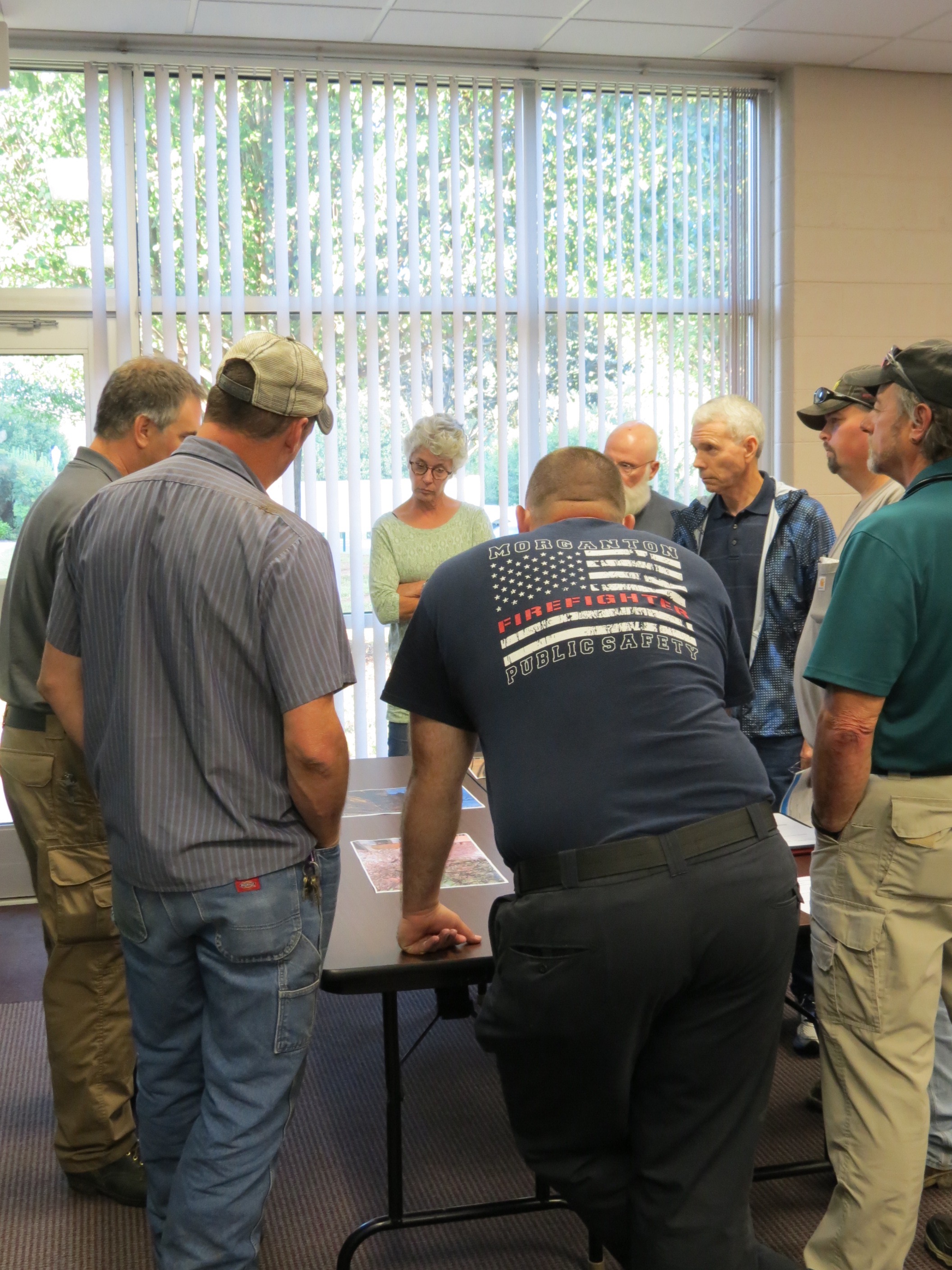 A group of people standing around a table, bent over, looking at maps on the table.