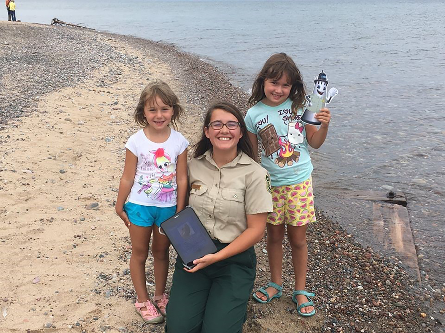 Photo: Two children pose at lake's edge with a Forest Service employee.
