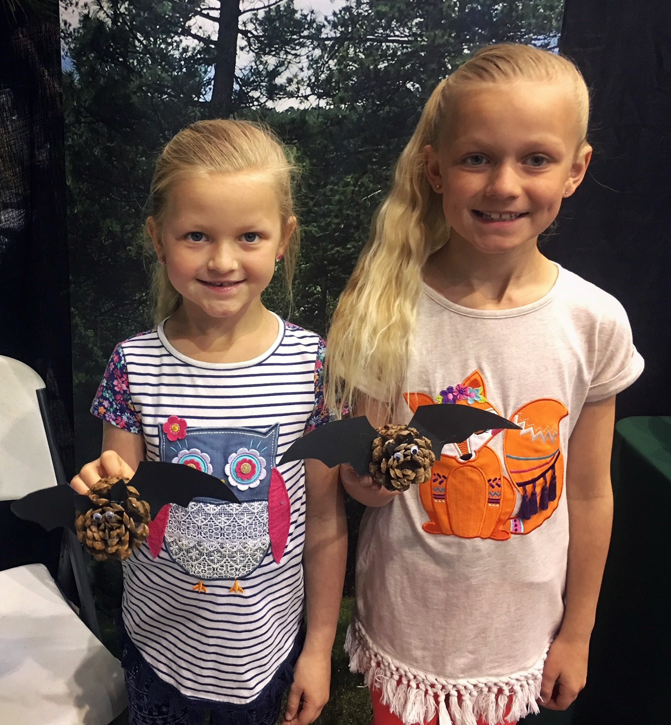 Photo: Two girls hold up bats made of pine cones.