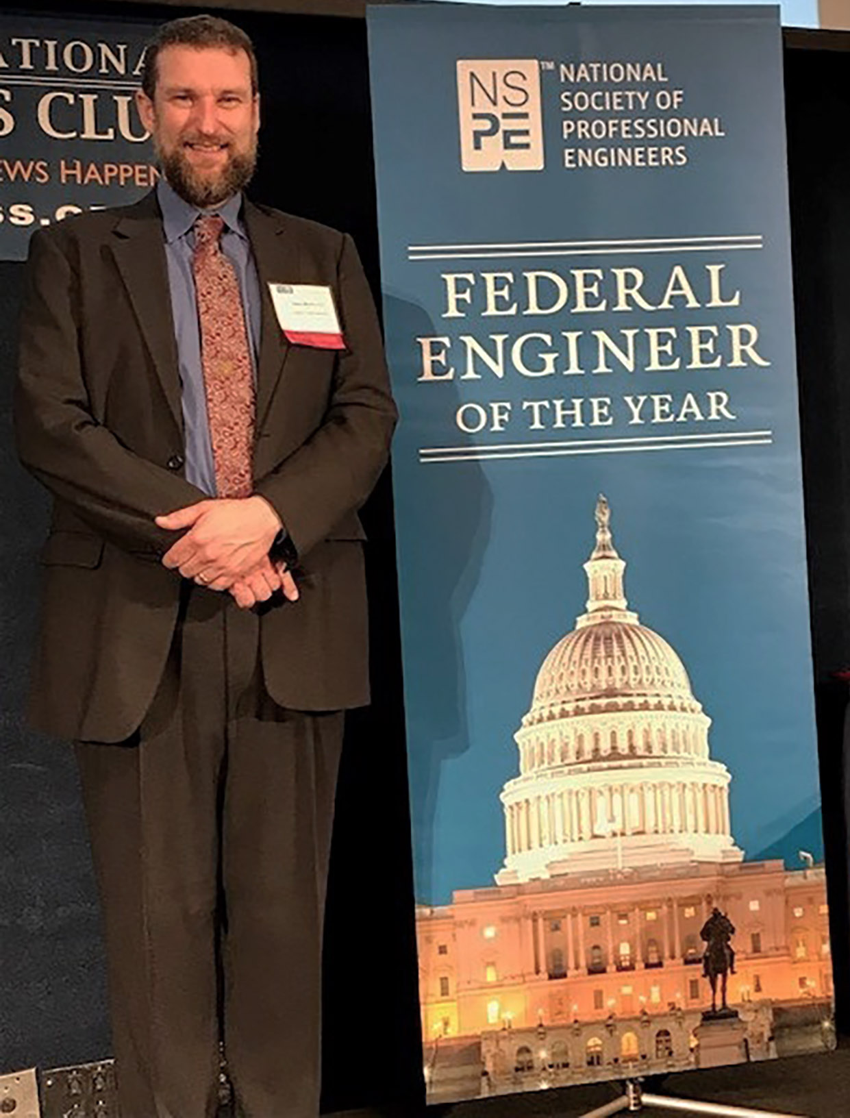 Photo: Man standing next to banner bug. Banner has image of U.S. Capitol at night below the text Federal Engineer of the Year.