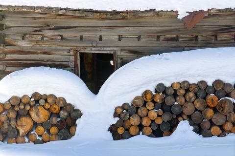 Snow covered firewood cut and stacked against the side of an old wood structure