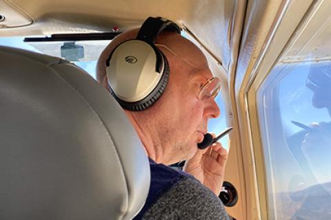 A person in sitting in a flying aircraft looking out the right window while appearing to talk in the microphone of a headset.