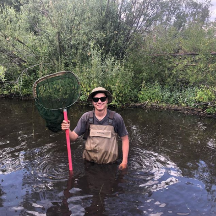 Matt Lugo waist-deep in river holding large net.