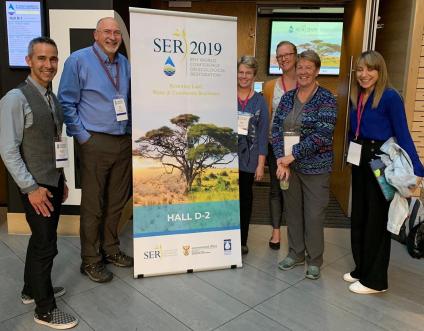 Presenters surrounding banner for seed symposium.