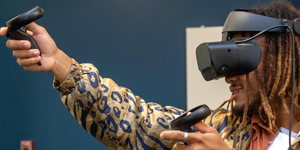 A person using virtual reality hardware, including a headset and two hand devices, in a conference room.