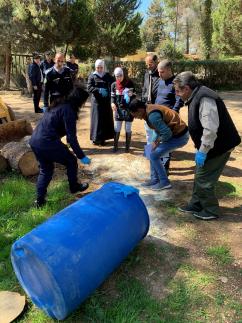 Group of men and women standing around a blue barrell