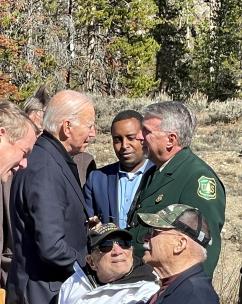 Frank Beum in Forest Service formal uniform shakes hands with President Biden. In foreground are two veterans of the World War II 10th Mountain Division.
