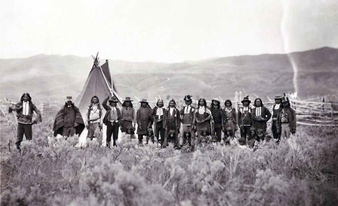 Shoshone men standing in a line in front of a tipi in Wyoming.