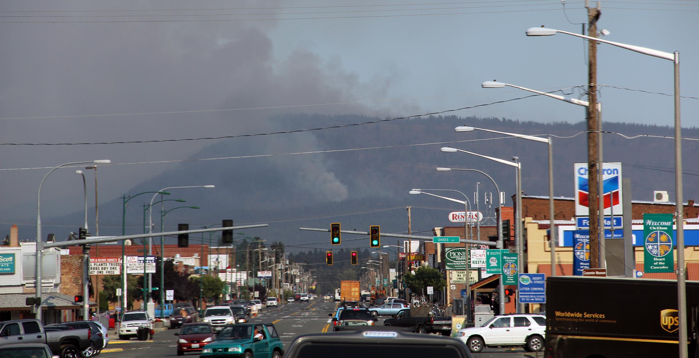 Busy city intersection with smoke coming off mountain in background