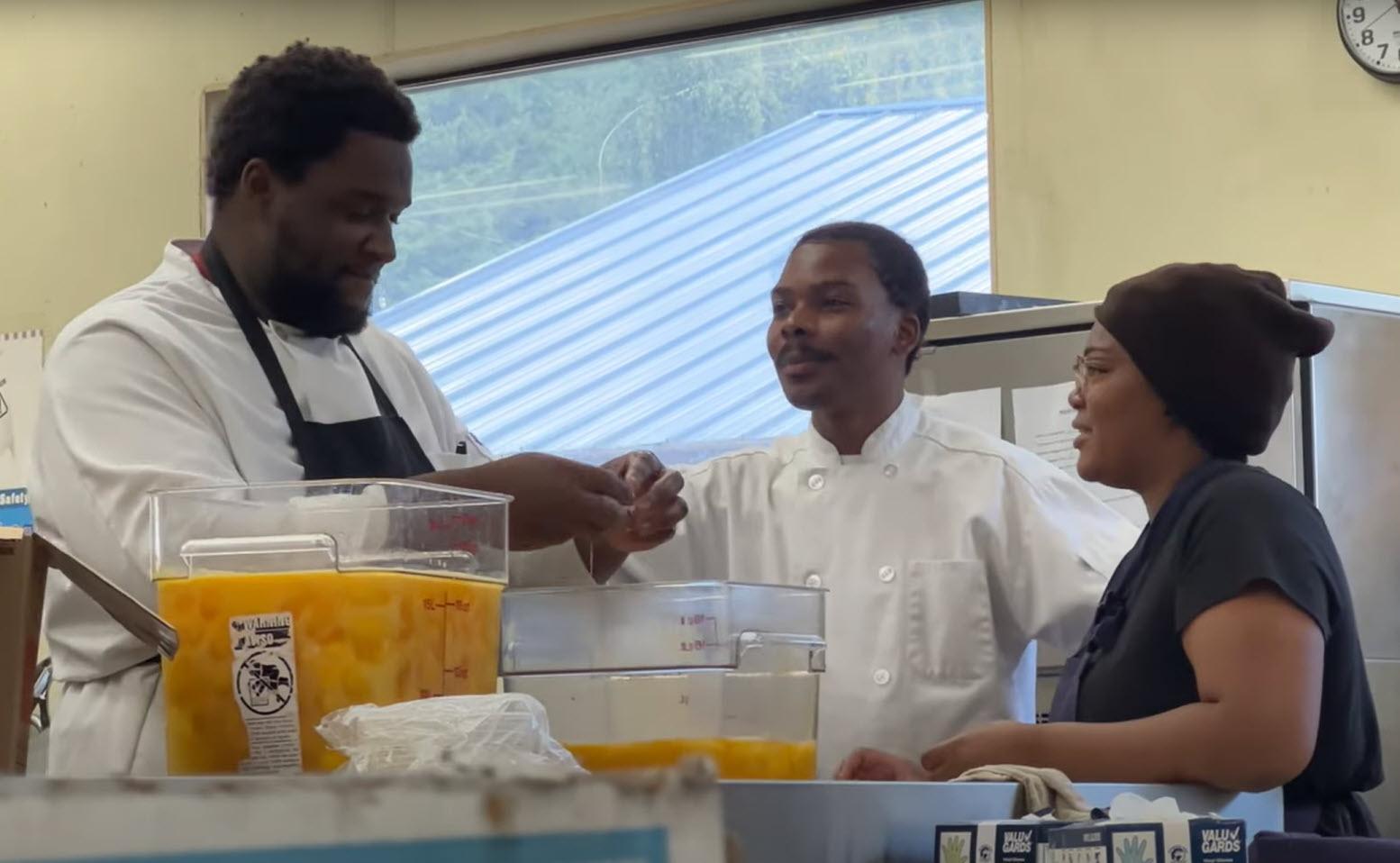 Three culinary specialists speak to each other while prepping eggs in a cafeteria kitchen.