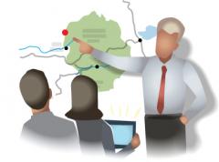 Avatar of a faceless human character pointing at a map on the wall while two other sitting avatar humans watch.