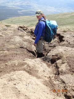 A trails design assistant stands in an erosion area in a mountain peak