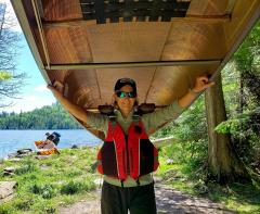 Connie Cummins carrying a canoe over her head in the great outdoors.