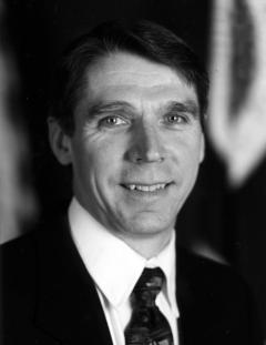 Black and white portrait: Mike Dombeck in suit jacket and tie.