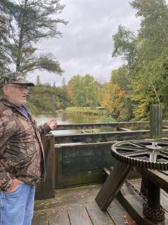 Older man standing on a wooden platform, next a large metal gear