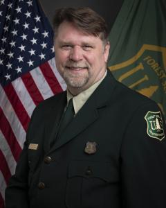 Portrait of acting Associate Chief Chris French in formal Forest Service uniform. Posed in front of American and Forest Service flags.