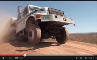 A picture showing a large tanker trunk climbing up and over a small hill on a dirt road.
